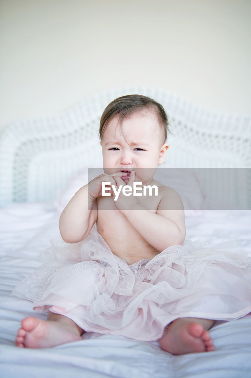 Full length portrait of cute baby girl crying on bed