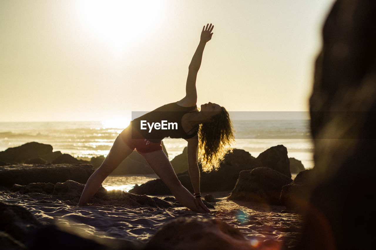 Woman exercising on beach during sunset