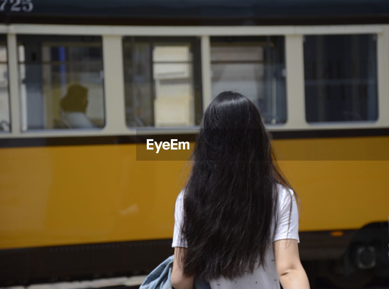 Rear view of woman with long hair walking towards train at platform