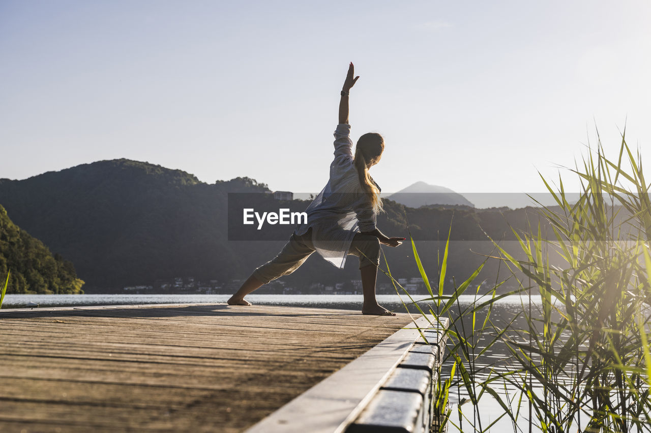 Mature woman doing yoga on jetty by lake