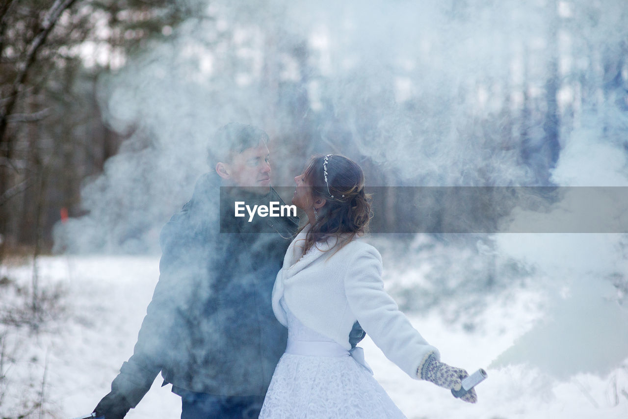 Close-up of couple with distress flare standing against tree during winter