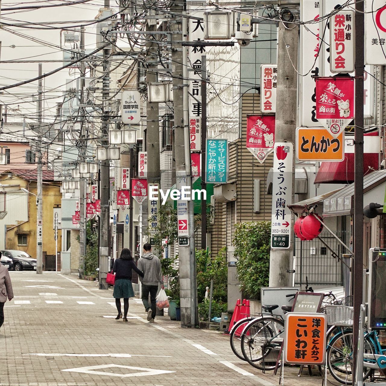 REAR VIEW OF MAN WALKING ON STREET AGAINST BUILDINGS