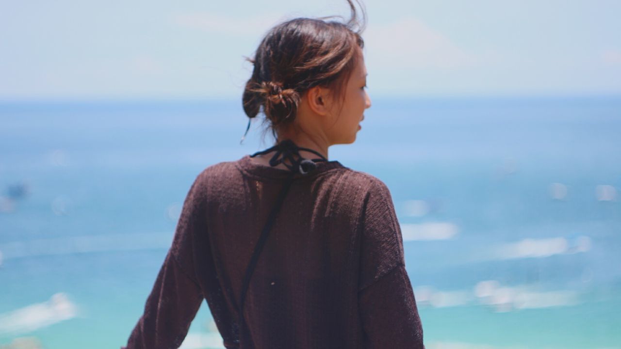 Rear view of young woman standing against sea on sunny day