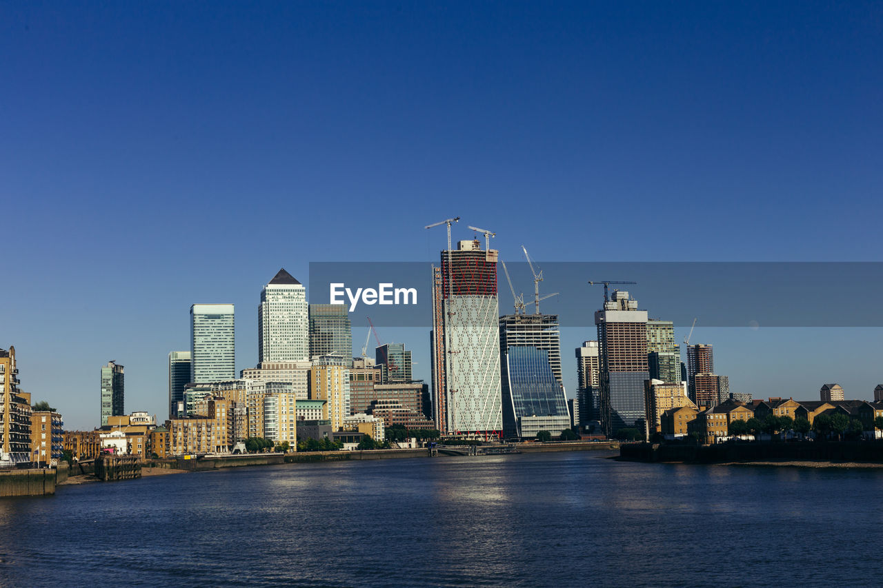 RIVER AMIDST BUILDINGS AGAINST CLEAR BLUE SKY