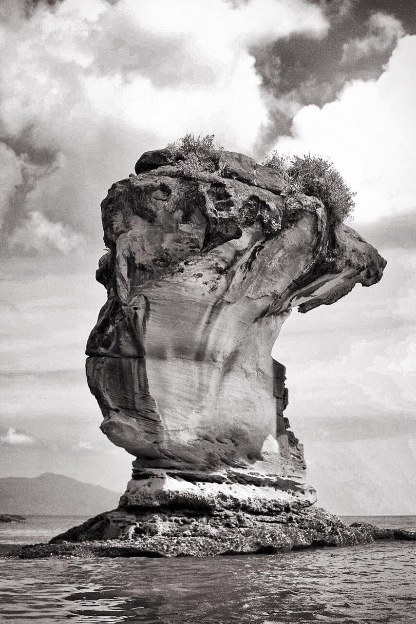 View of rock formation in sea against cloudy sky