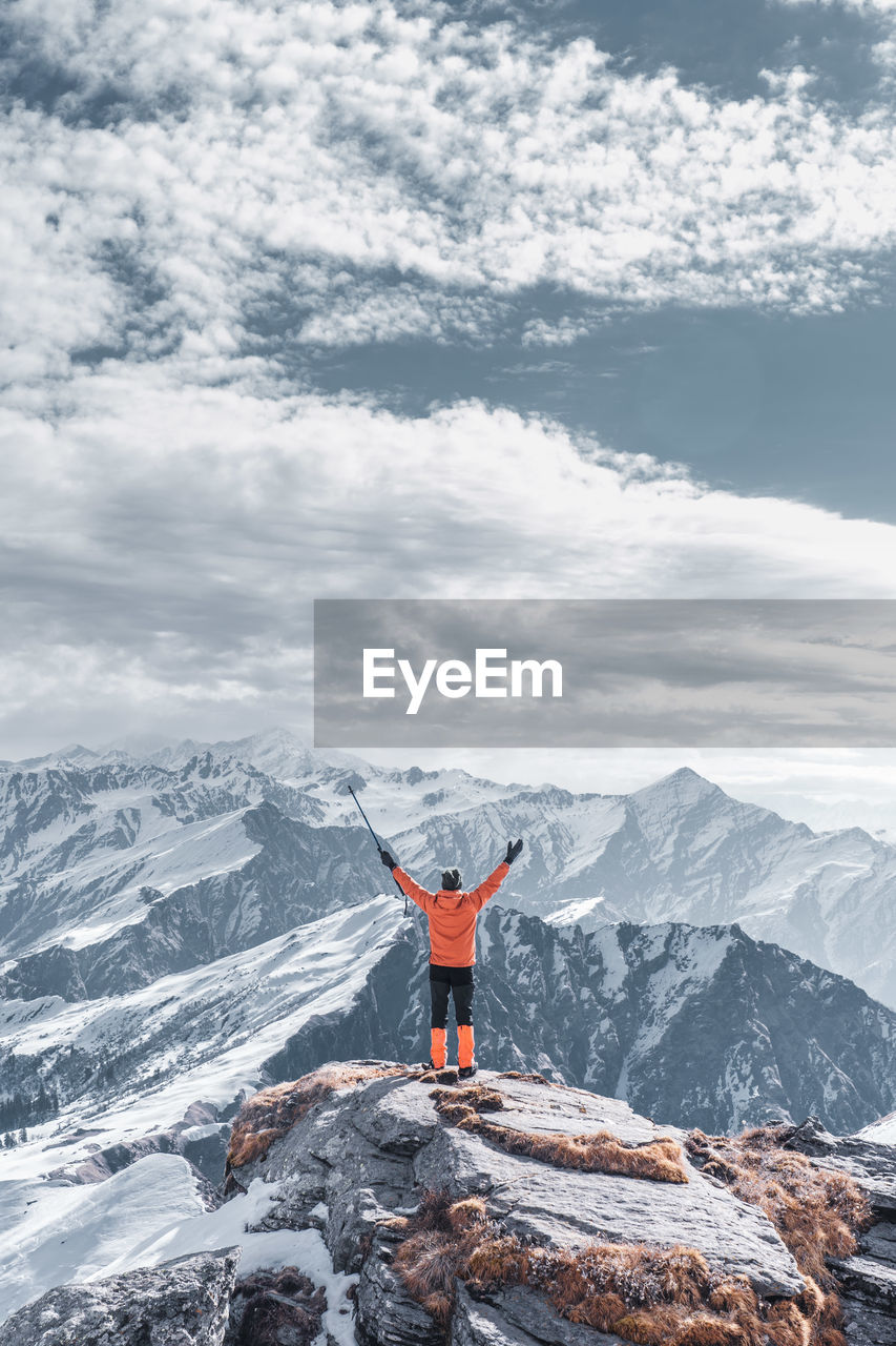 Rear view of man standing on cliff against snow capped mountain