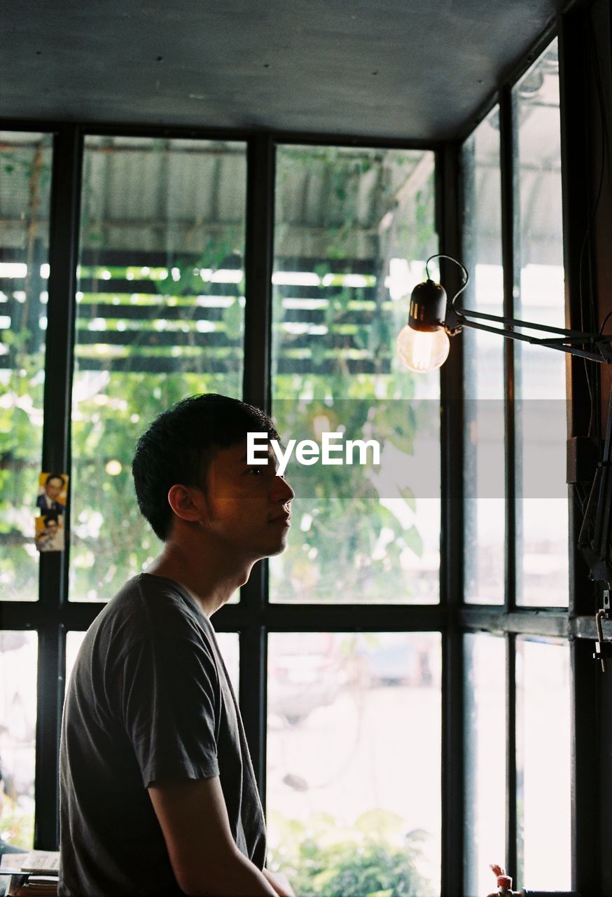 Side view of young man looking at illuminated light bulb by window