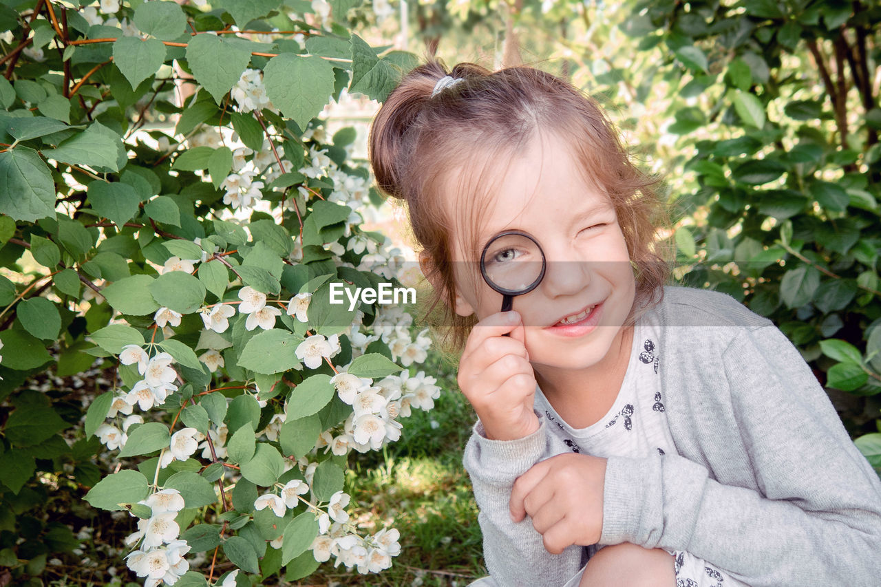 Portrait of little girl 4-7 years old with magnifying glass in examining leaves in park 