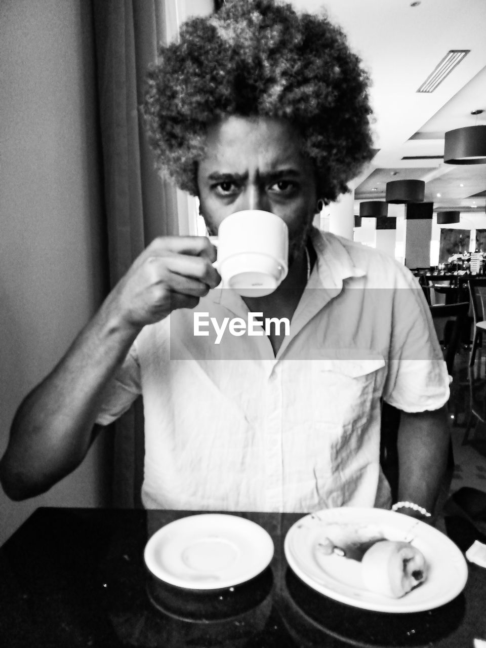 black, one person, white, adult, black and white, food and drink, monochrome, indoors, person, monochrome photography, curly hair, portrait, human hair, clothing, front view, men, looking at camera, food, tableware, young adult, lifestyles, drink, coffee, waist up, cup, holding, human face, hairstyle, business, mug, table, refreshment, coffee cup, occupation, sitting