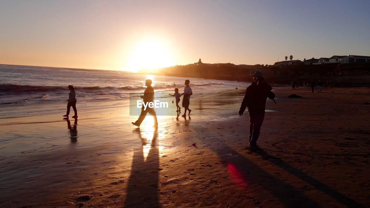 Silhouette people on beach against sky during sunset