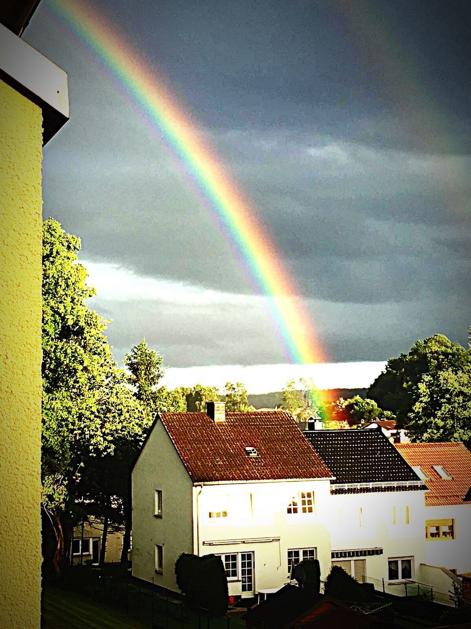 RAINBOW OVER HOUSES AGAINST CLOUDY SKY