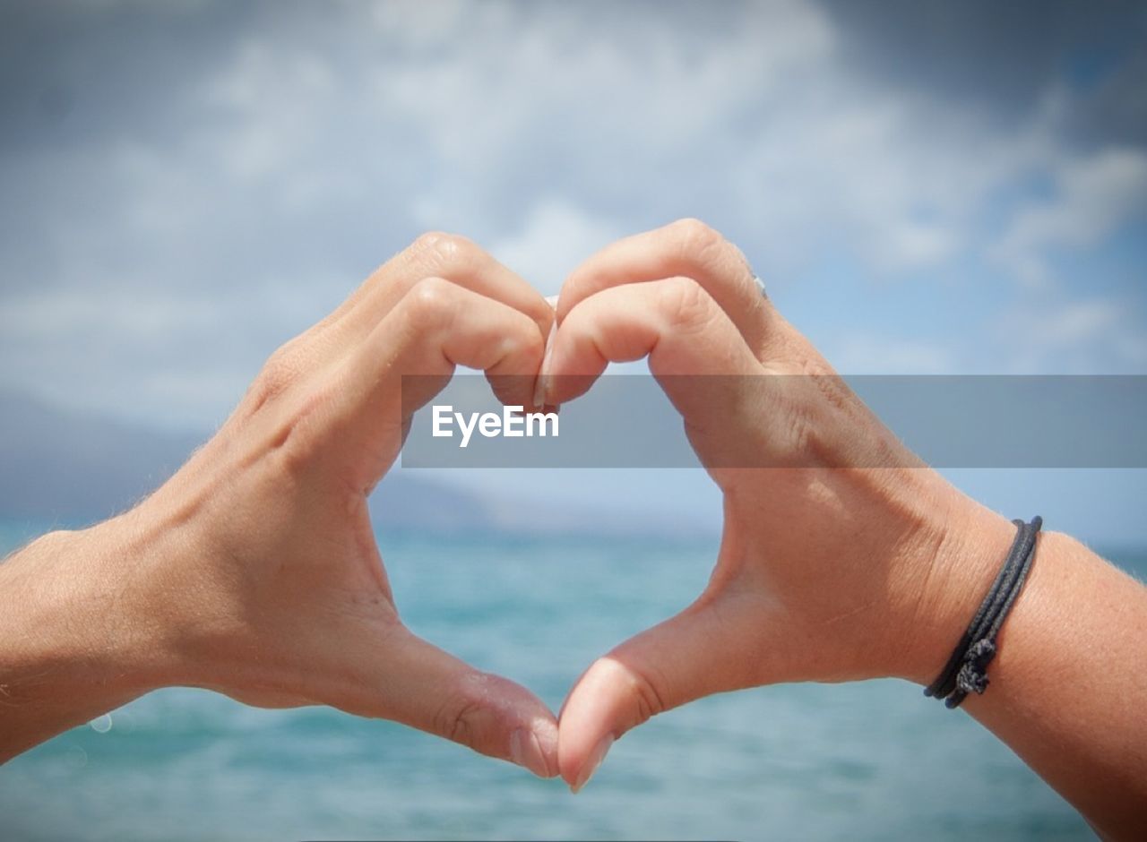 Cropped image of hands making heart shape against sea