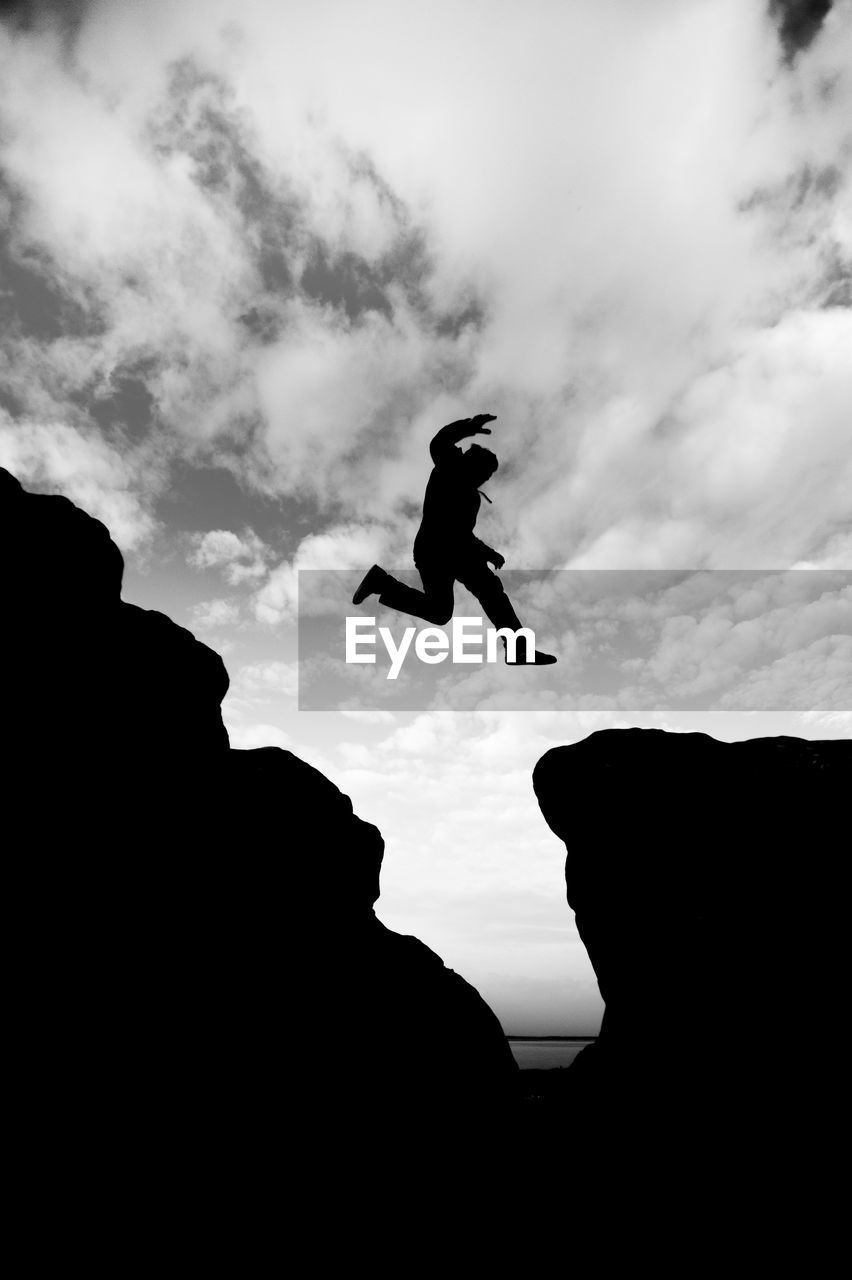 LOW ANGLE VIEW OF SILHOUETTE MAN JUMPING ON ROCK