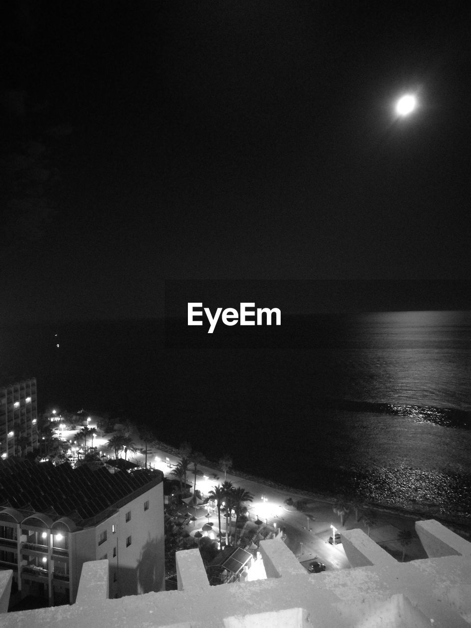 HIGH ANGLE VIEW OF ILLUMINATED CITY BY SEA AT NIGHT