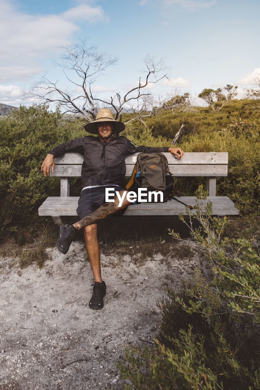 Full length of hiker with backpack wearing straw hat while sitting on bench at wilsons promontory national park