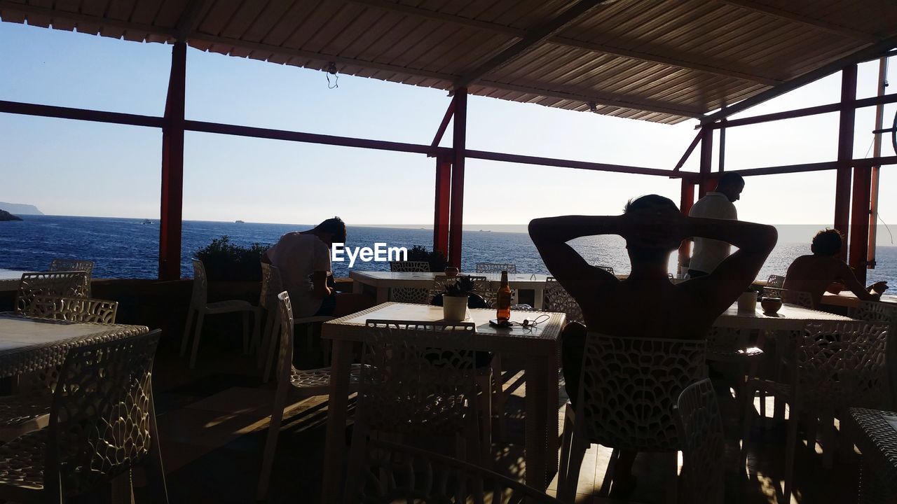 PEOPLE STANDING IN RESTAURANT BY SEA AGAINST SKY