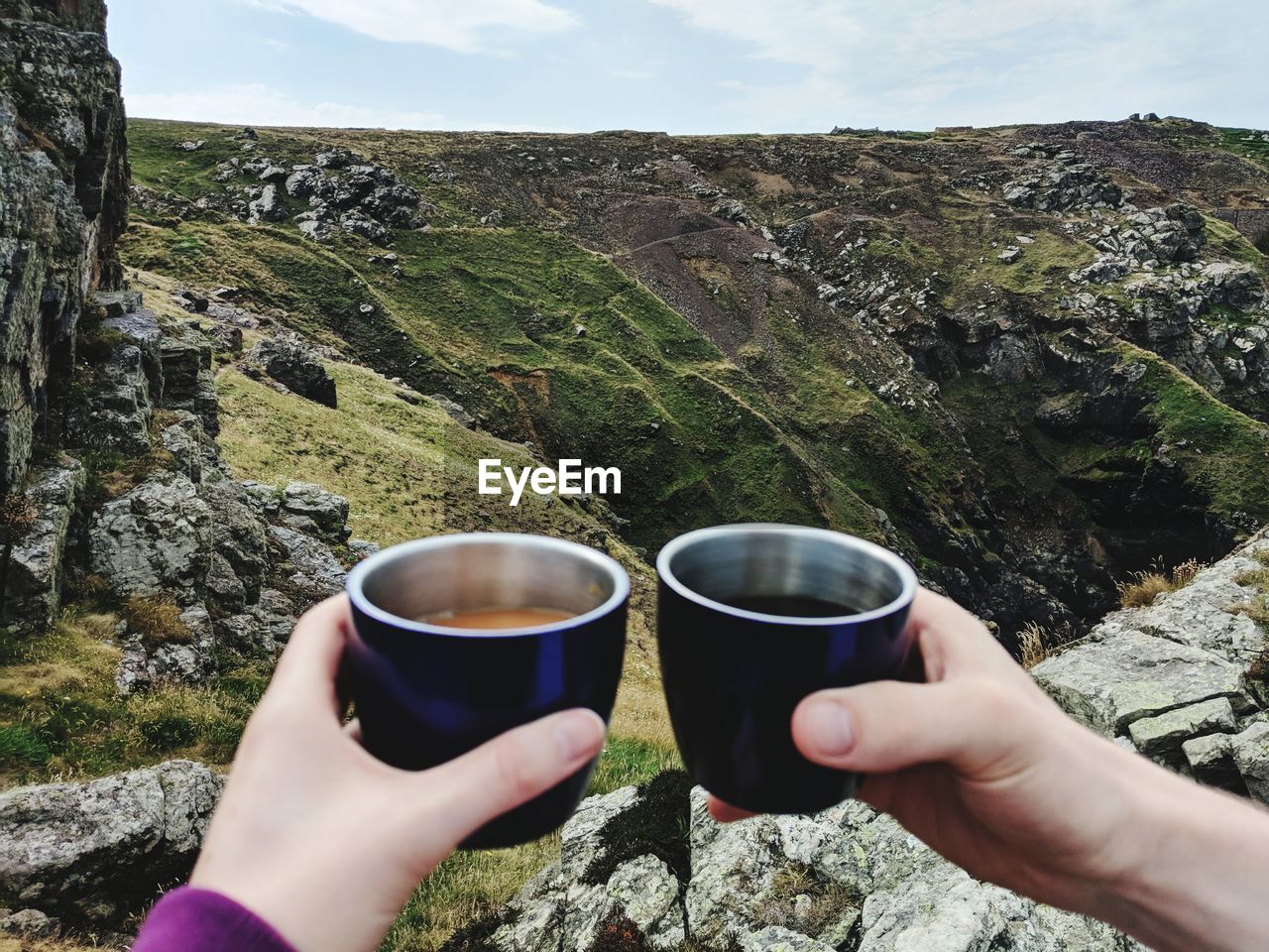 Cropped hands of people holding drinks against mountain range