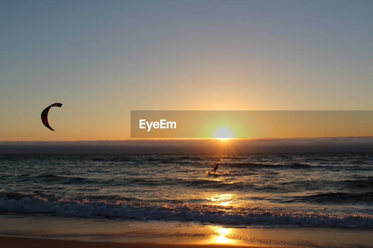 Person kiteboarding on sea against sky during sunset