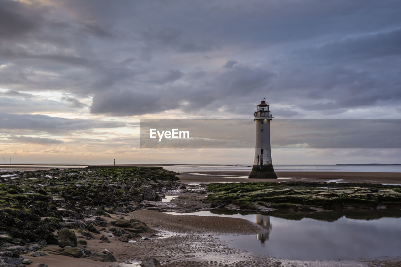 Lighthouse amidst sea and buildings against sky