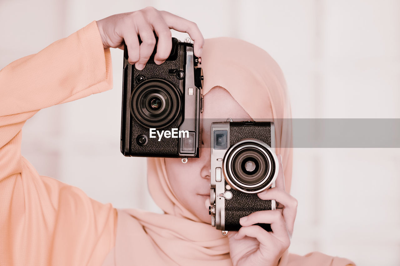 Close-up of teenage girl holding cameras against face