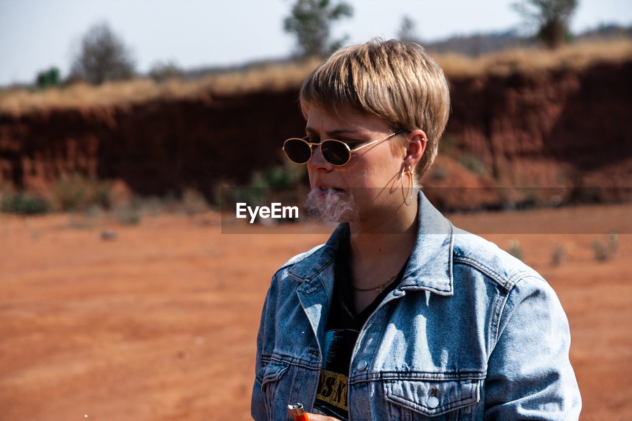 Young woman wearing sunglasses smoking while standing outdoors