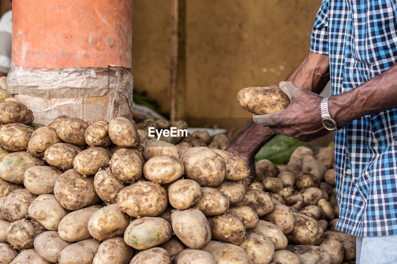 Midsection of male vendor selling potatoes at market