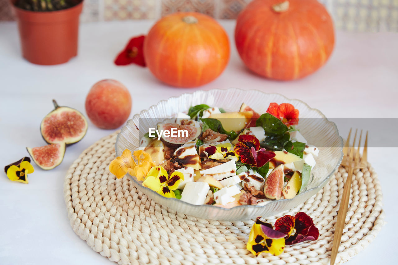 Autumn breakfast - vegetarian salad with feta, edible flowers, figs, peach, basil on ceramic tile 