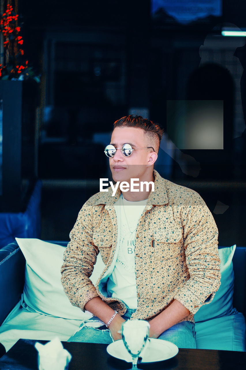 Young man wearing sunglasses while sitting on table