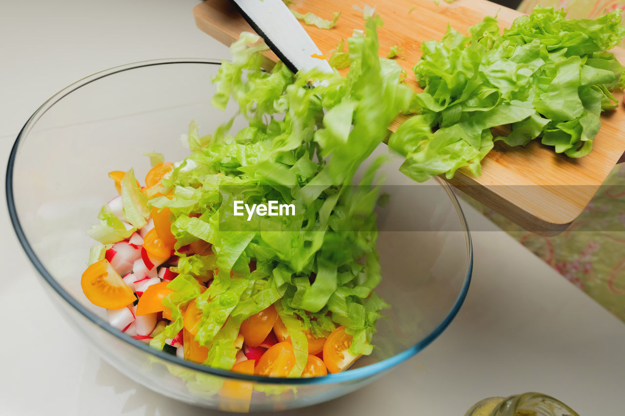 Salad with greens, tomatoes and radishes in a glass bowl. sliced lettuce on a board with a knife