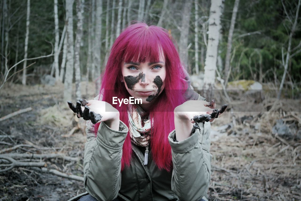 Portrait of redhead woman with mud on face crouching in forest