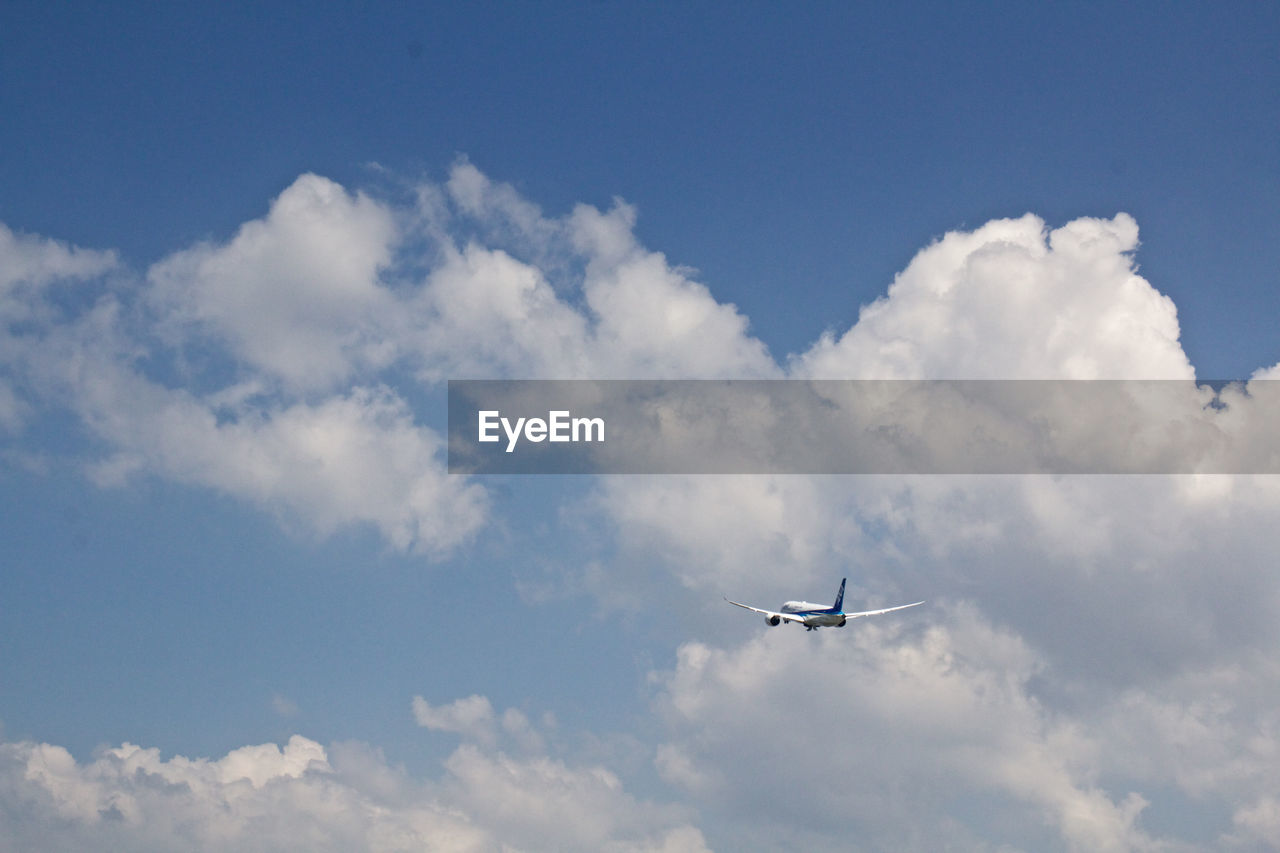 LOW ANGLE VIEW OF AIRPLANE FLYING OVER CLOUDS