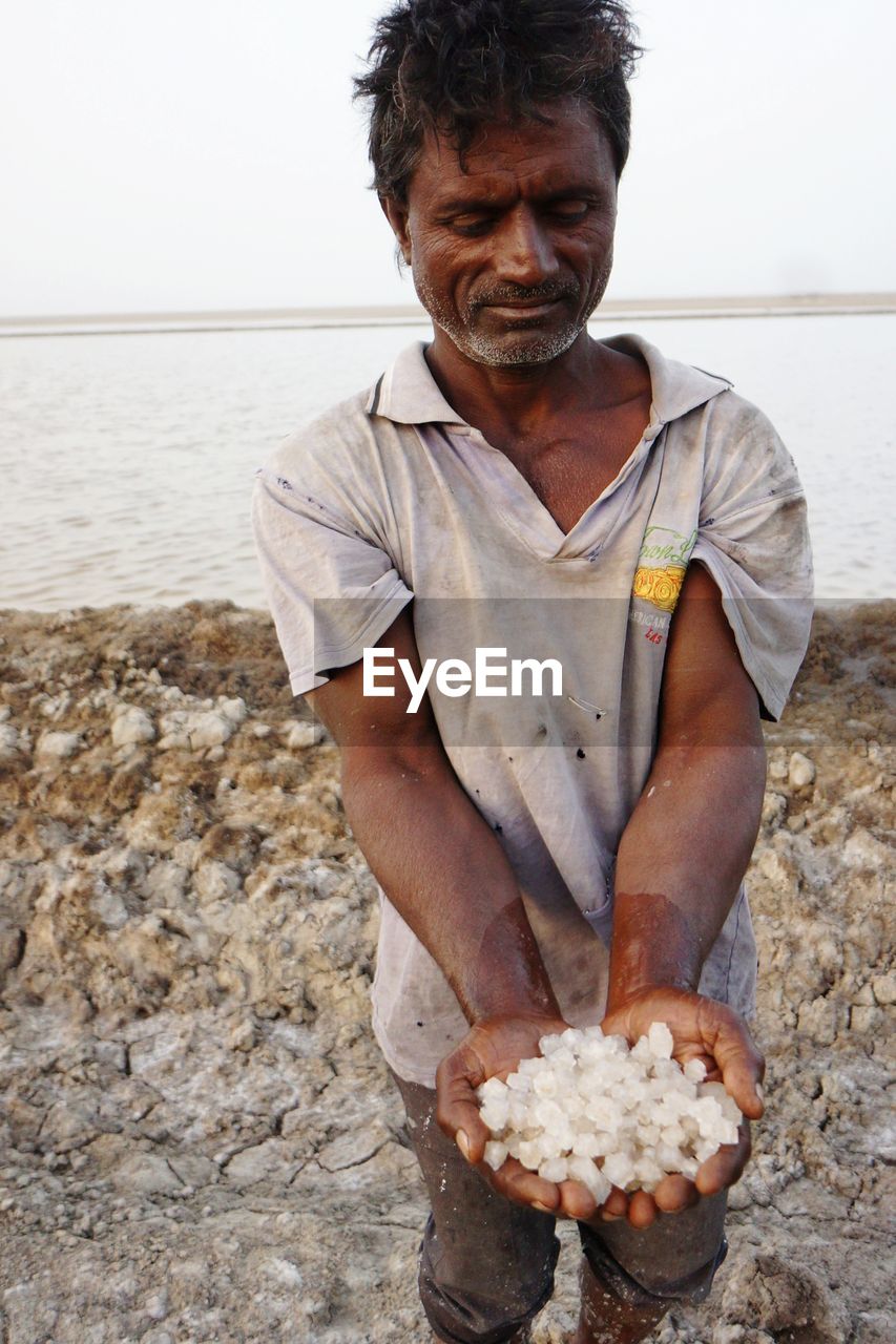 Mature man holding salt while standing at beach