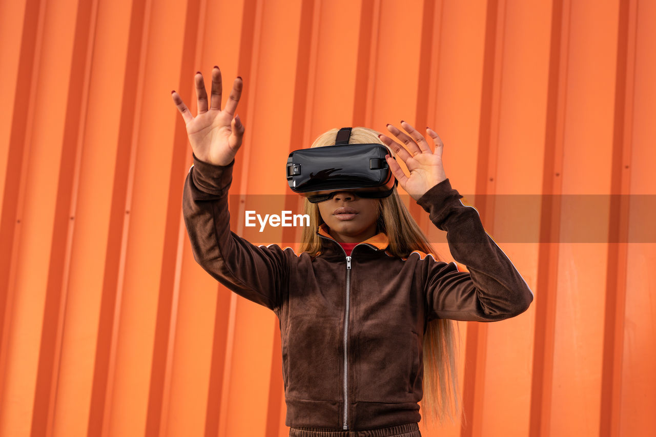 Pretty african american woman using virtual reality glasses on an orange background