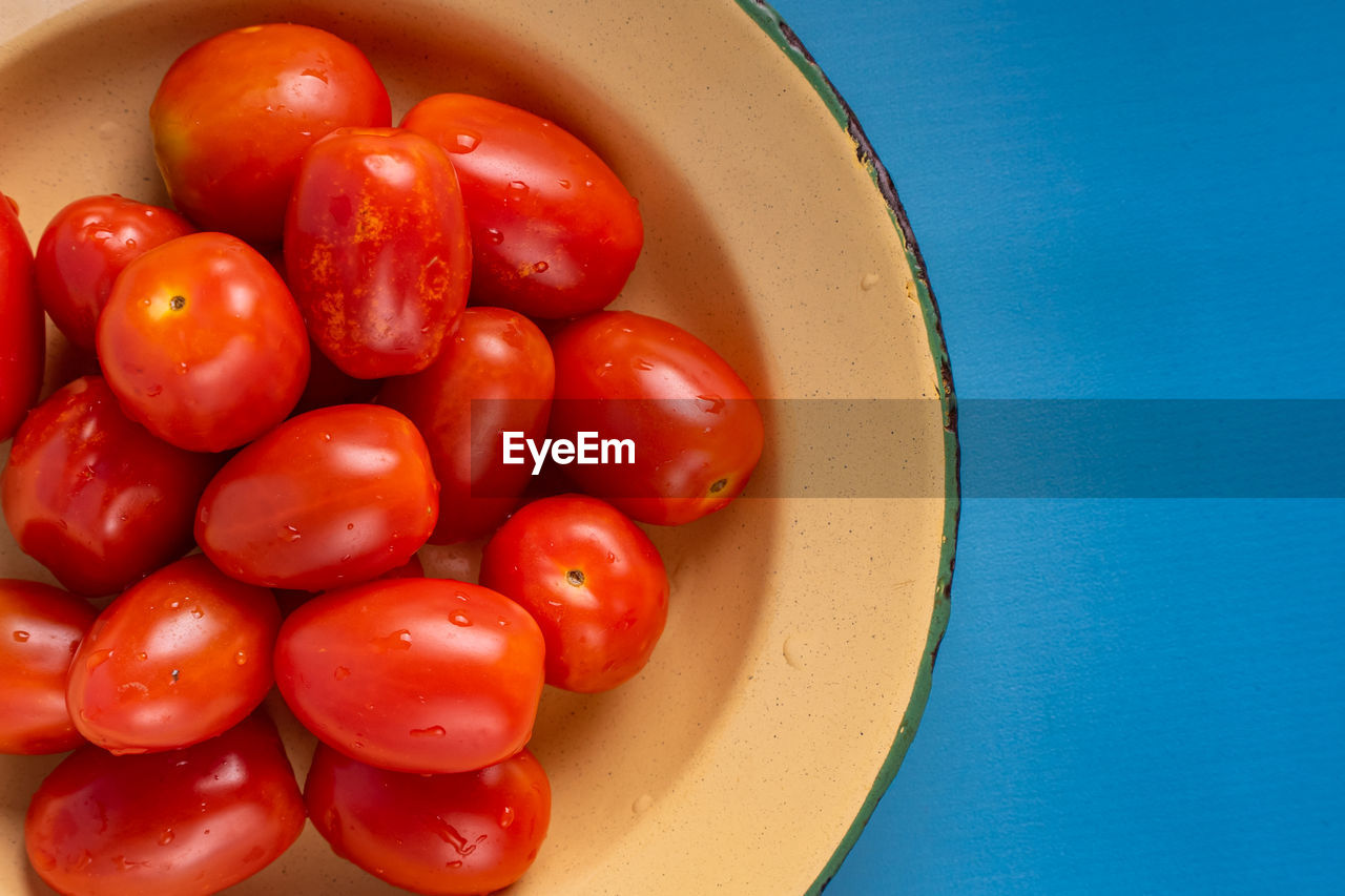 Group of fresh cherry tomatoes on rustic plate isolate in blue background. 