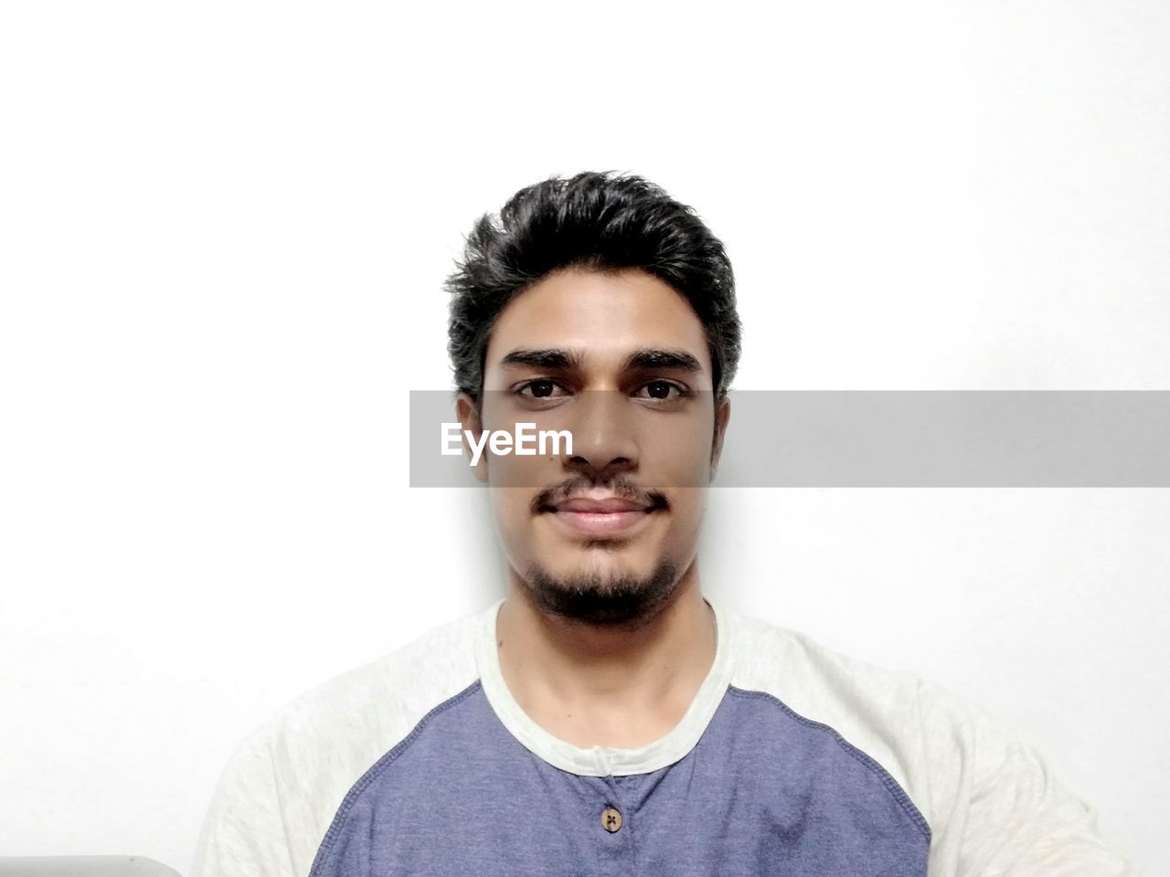 PORTRAIT OF SMILING YOUNG MAN OVER WHITE BACKGROUND