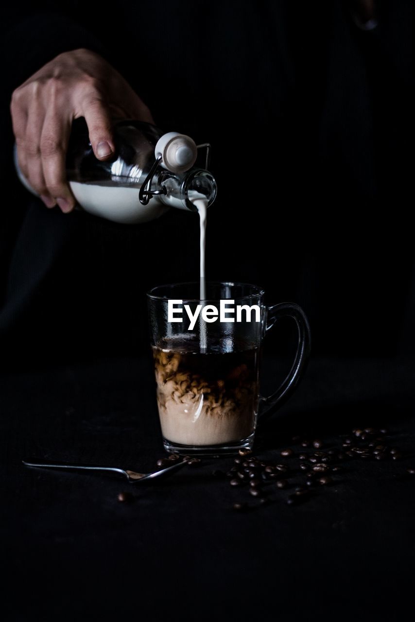 Cropped hand pouring milk in cup against black background