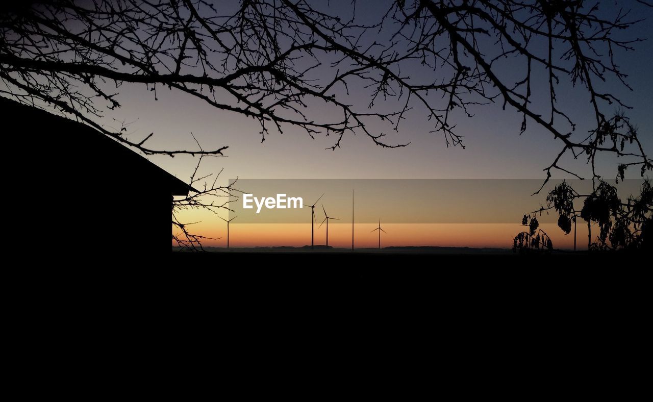 Silhouette trees and house against sky during sunset