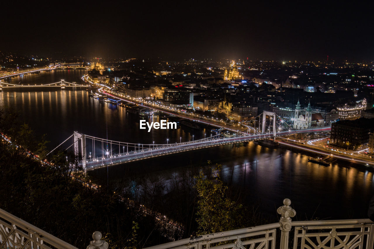 Illuminated bridge over river in city against sky at night