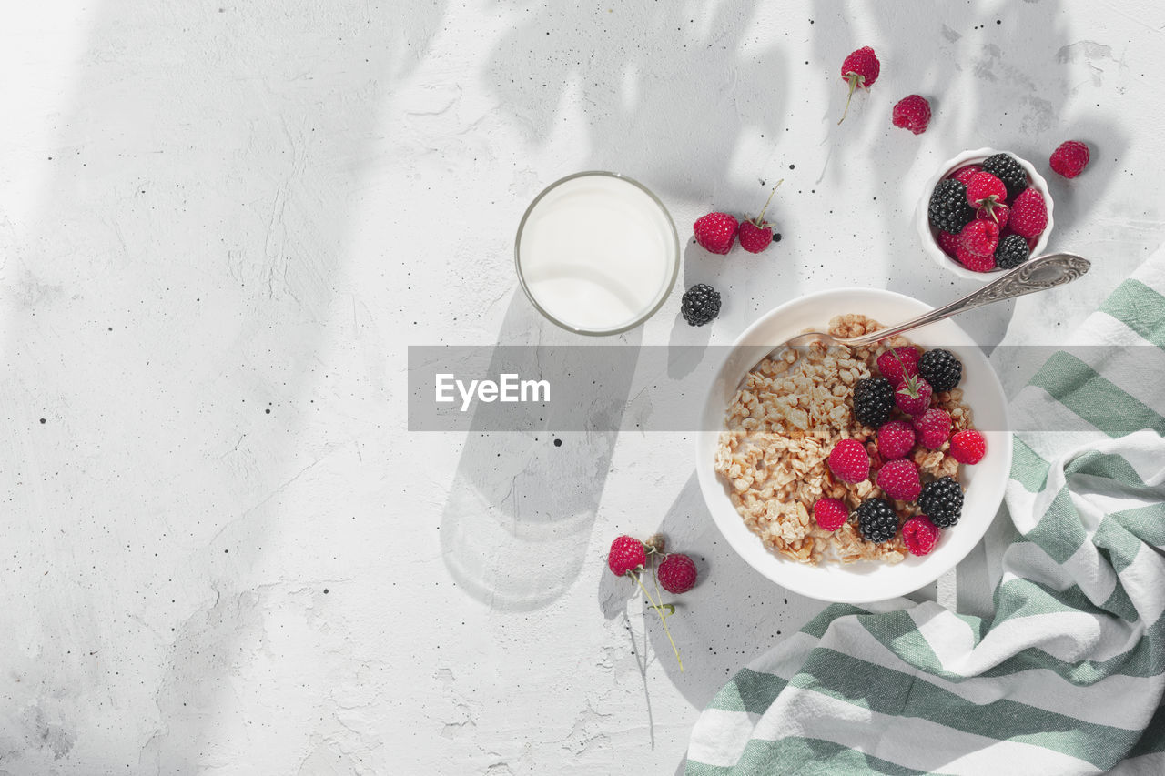 Morning healthy breakfast, white bowl full with granola, muesli, raspberry, blackberry on gray table