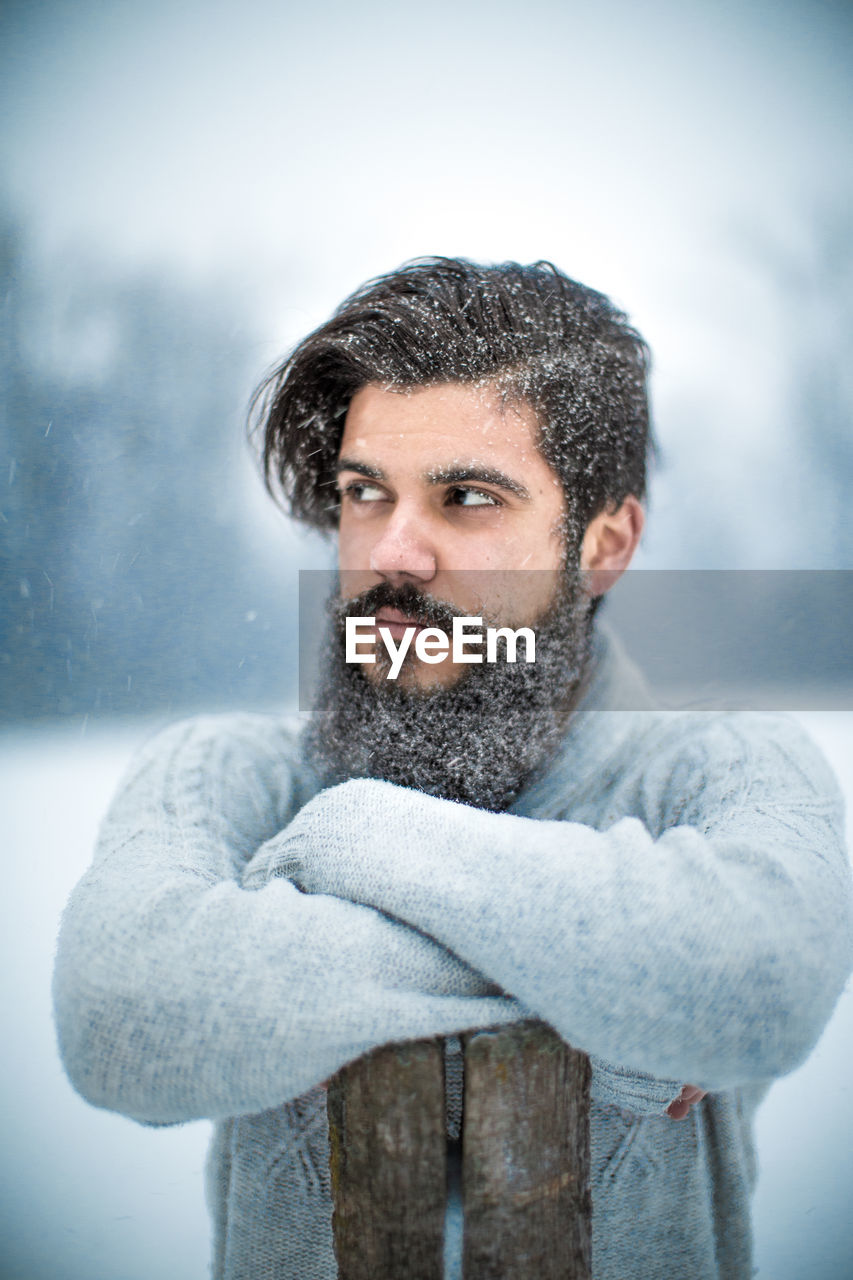 Young bearded man with arms crossed standing during snowfall
