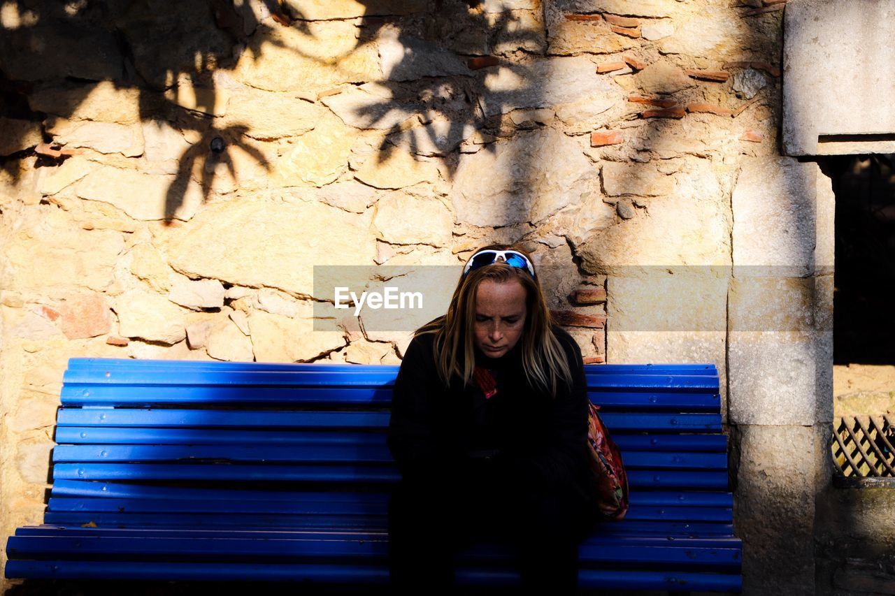 Thoughtful woman sitting on bench against wall in city