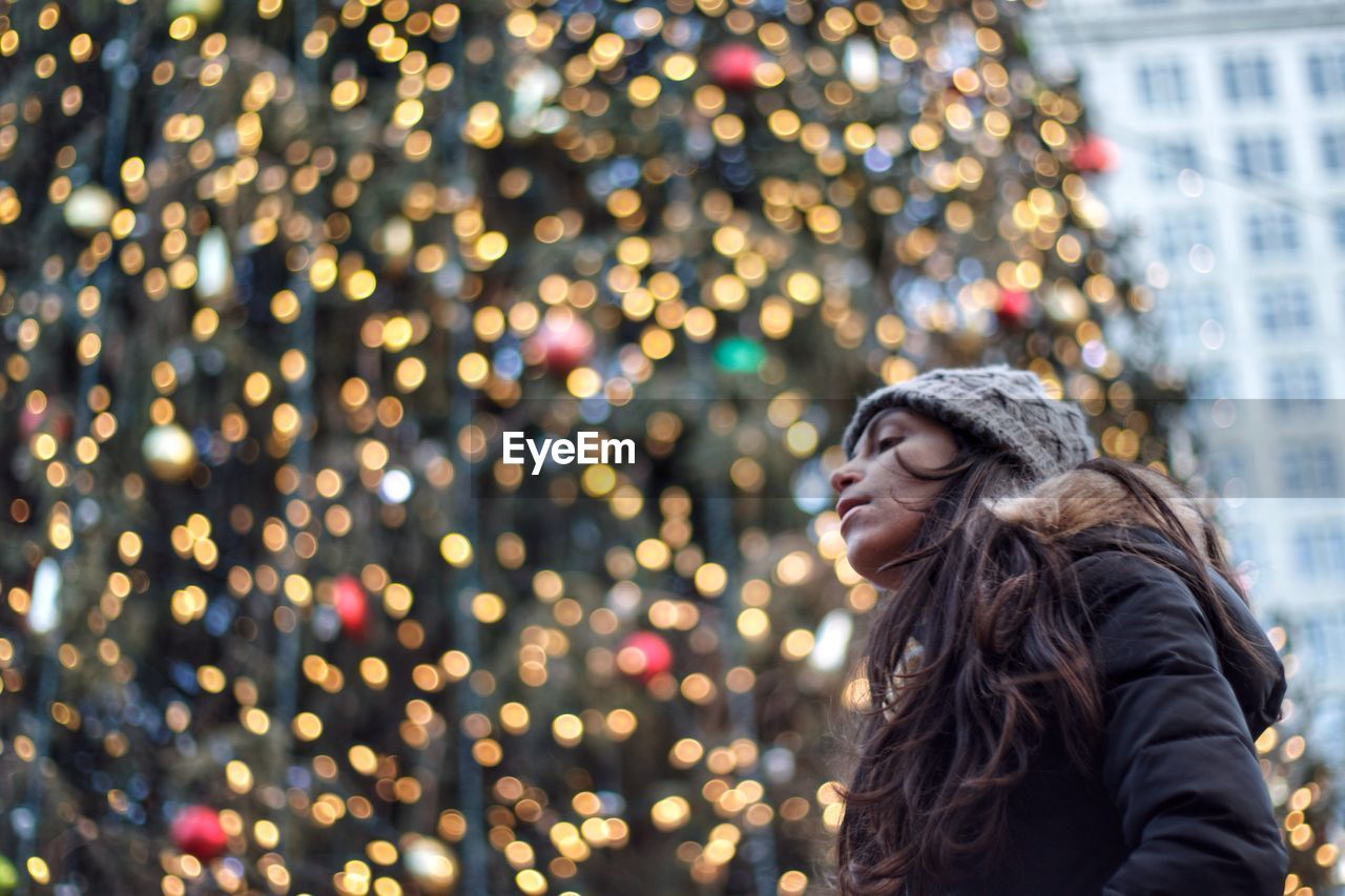 Woman looking at illuminated christmas tree in city during winter