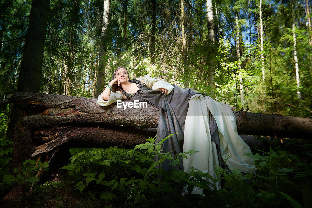 rear view of woman standing on tree trunk in forest