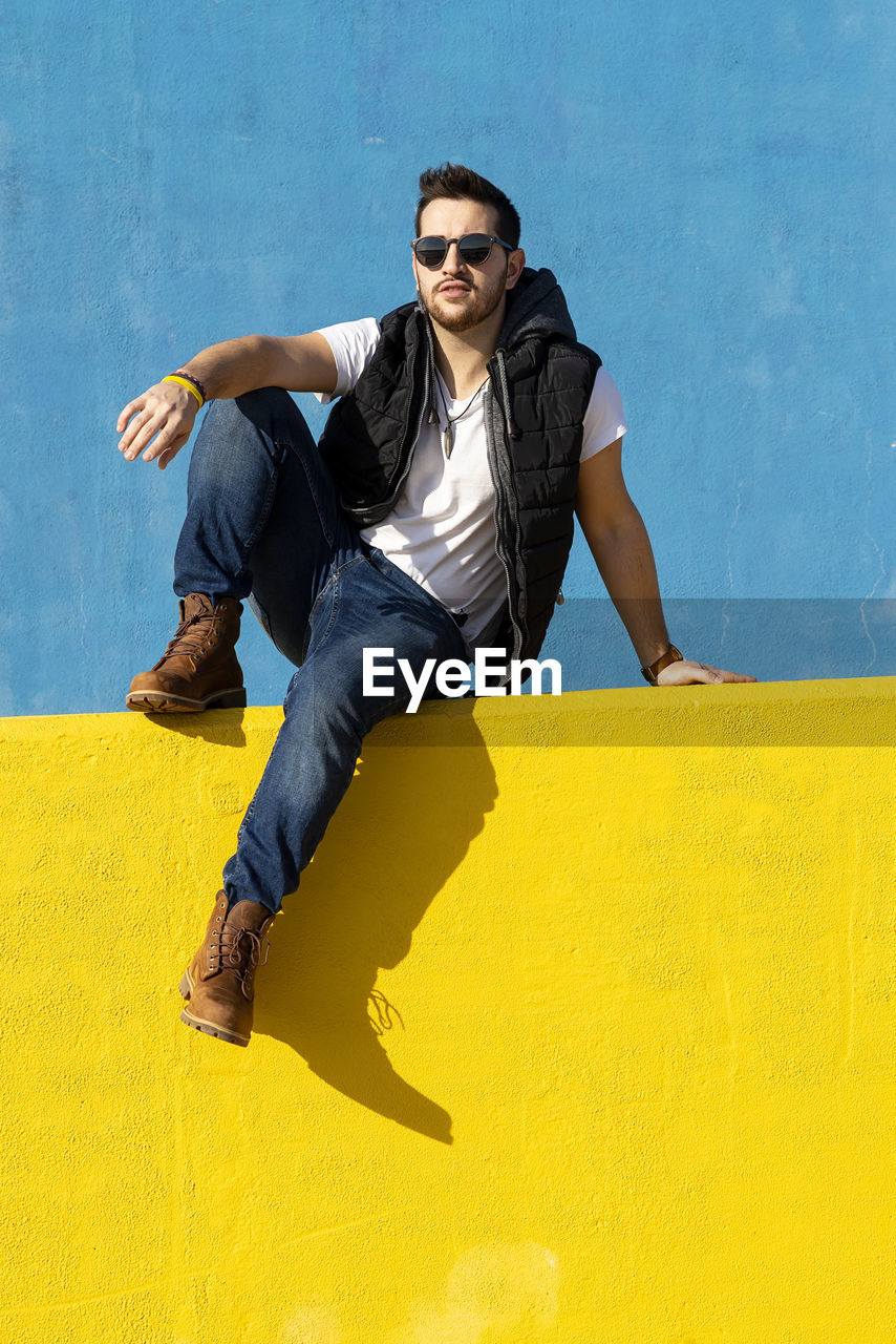 Bearded man in white t-shirt, jacket and jeans against blue background