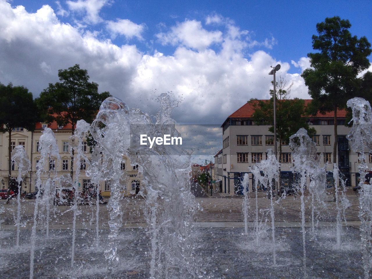 Fountains in city against cloudy sky