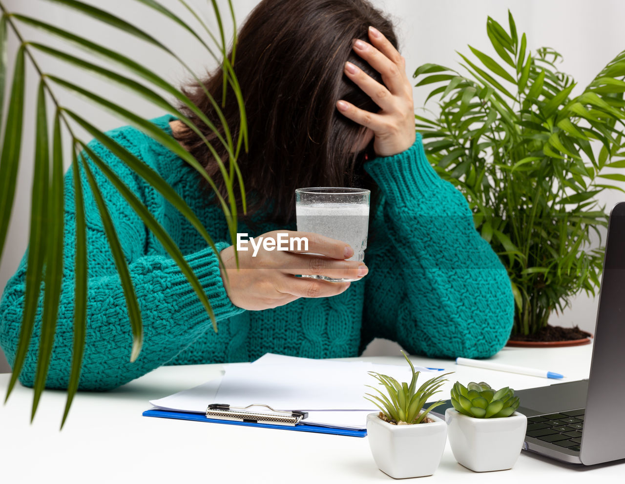 Woman in a sweater sits at the table with her head clasped in her hands, stress and 