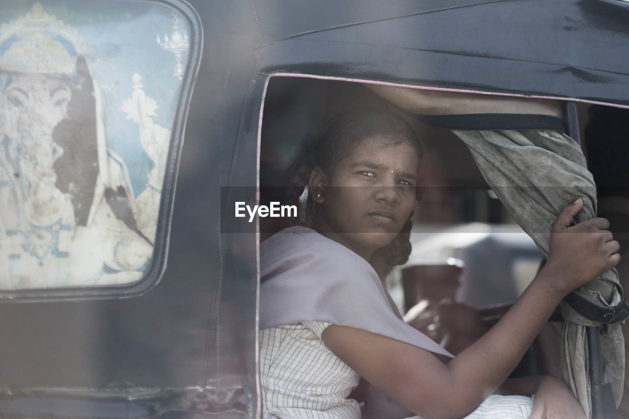 PORTRAIT OF YOUNG WOMAN SITTING BY CAR WINDOW