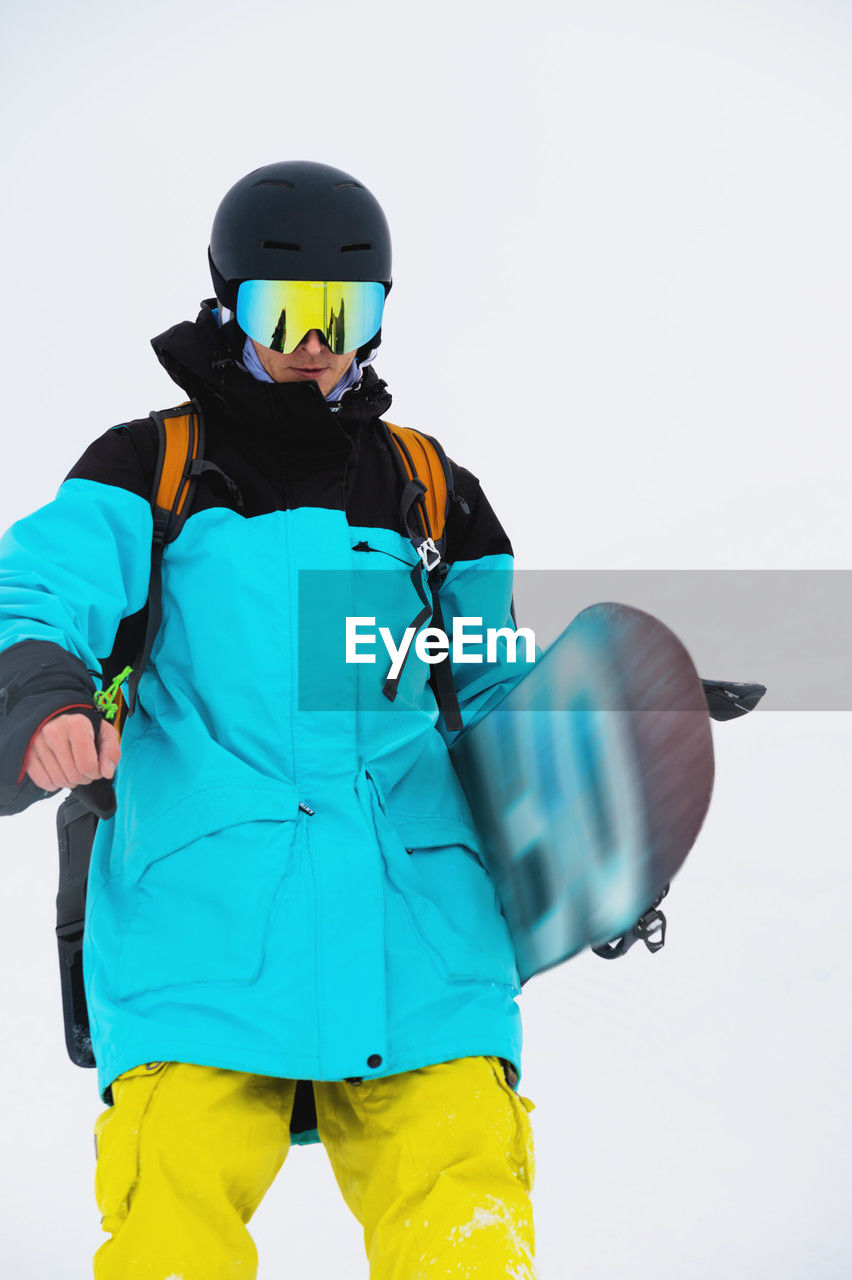 Close-up of a male snowboarder striding down the slope wearing a helmet and mask with his snowboard