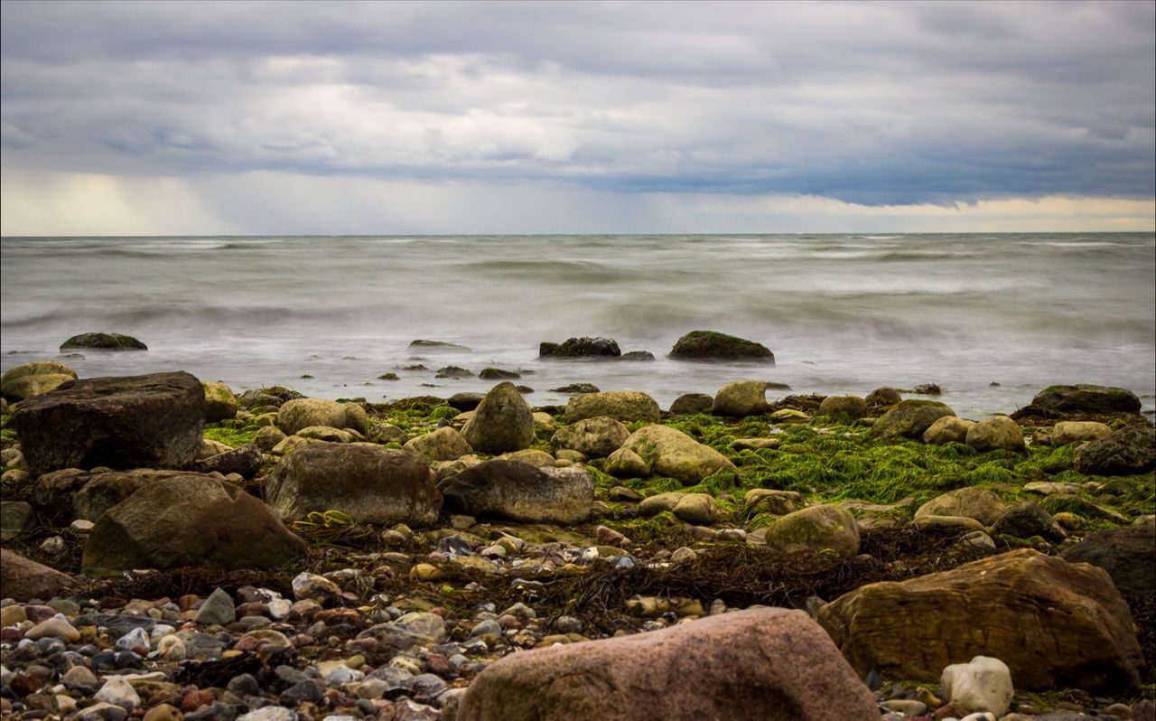 Rocks by sea against cloudy sky