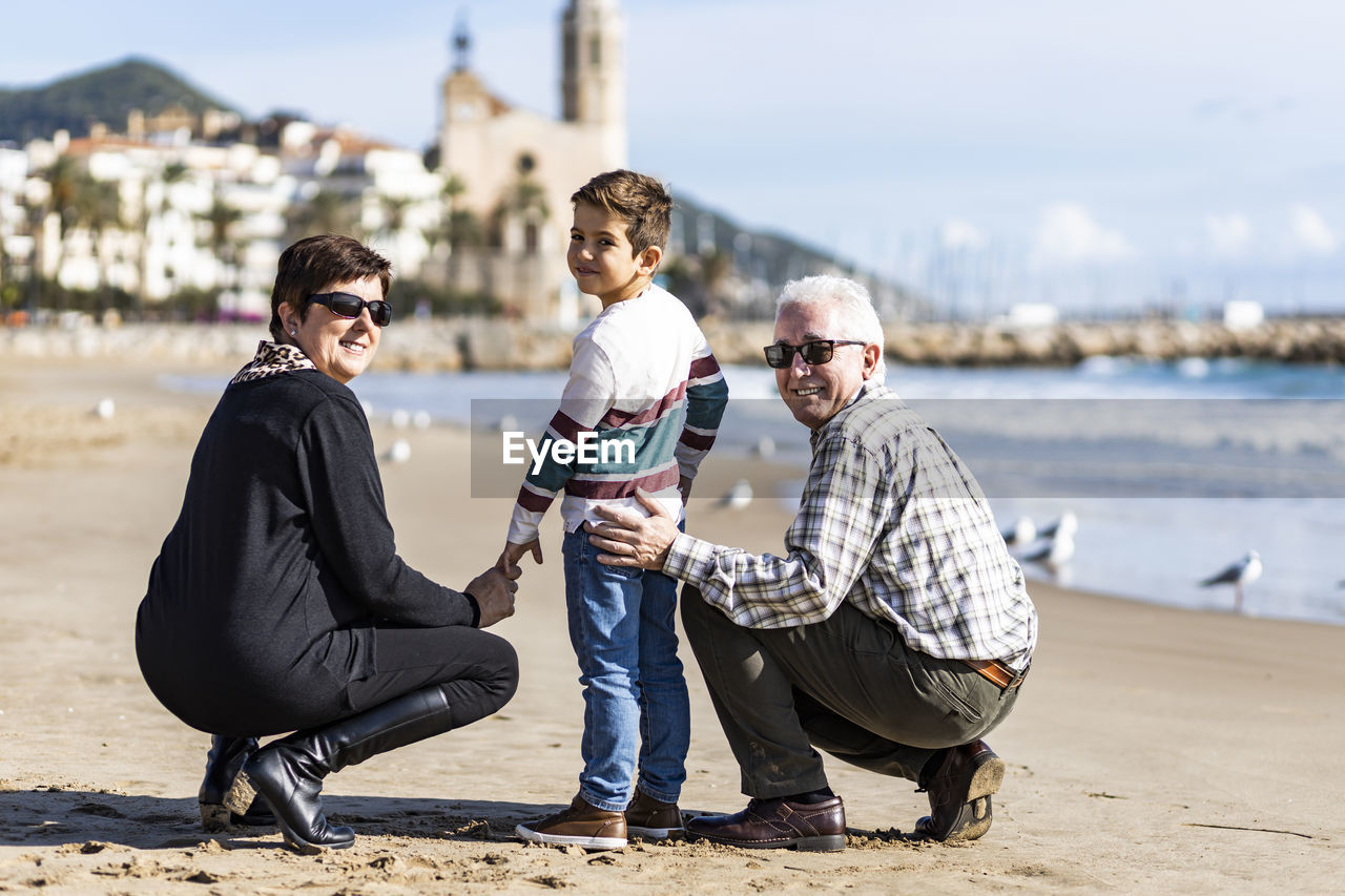 Portrait of happy grandparents with grandson crouching at beach